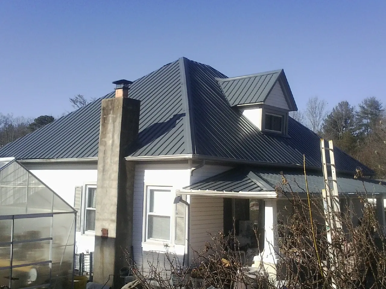 Dark blue standing seam metal roof on a white farmhouse with dormer in Oakes