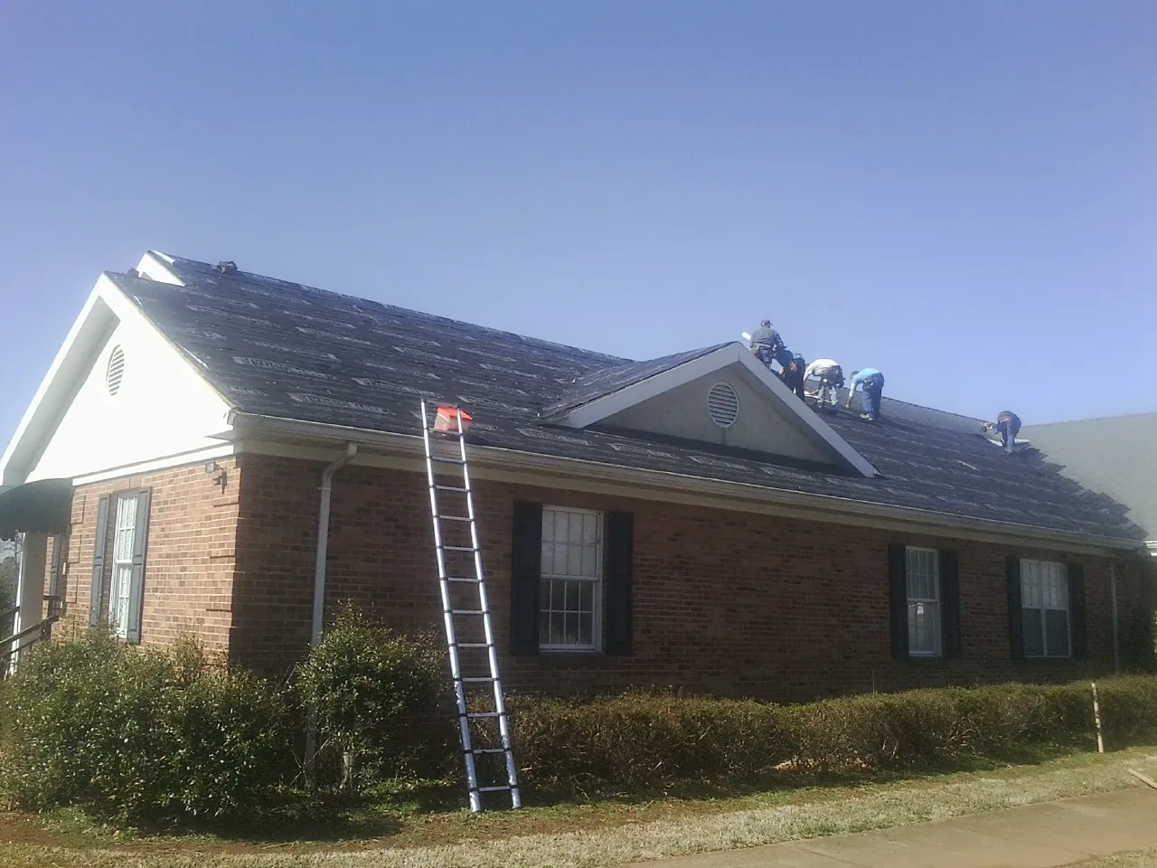Crew tearing shingles off a brick ranch roof with a ladder set — Metal Roof Repair work by our crew in Oakes