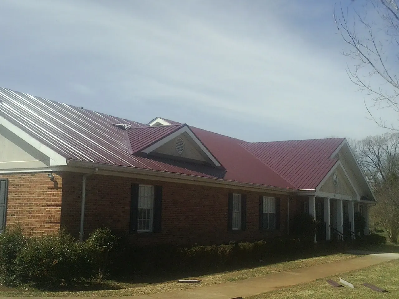 Red metal roof with gabled entries on a long brick building, from a Hail Damage Roof Repair job in Oakes