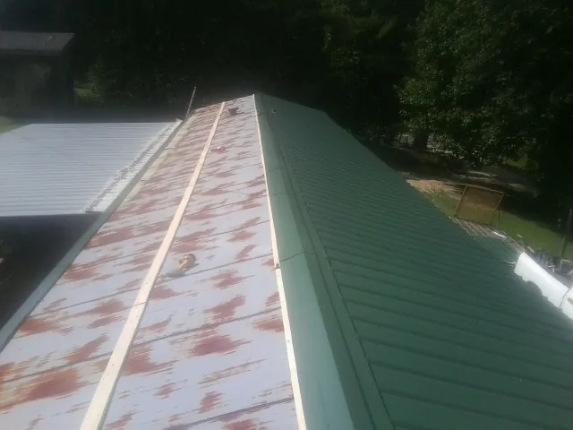 Old rusted panels beside newly installed green metal roofing — Wind Damage Roof Repair by Roofing Brothers in Oakes