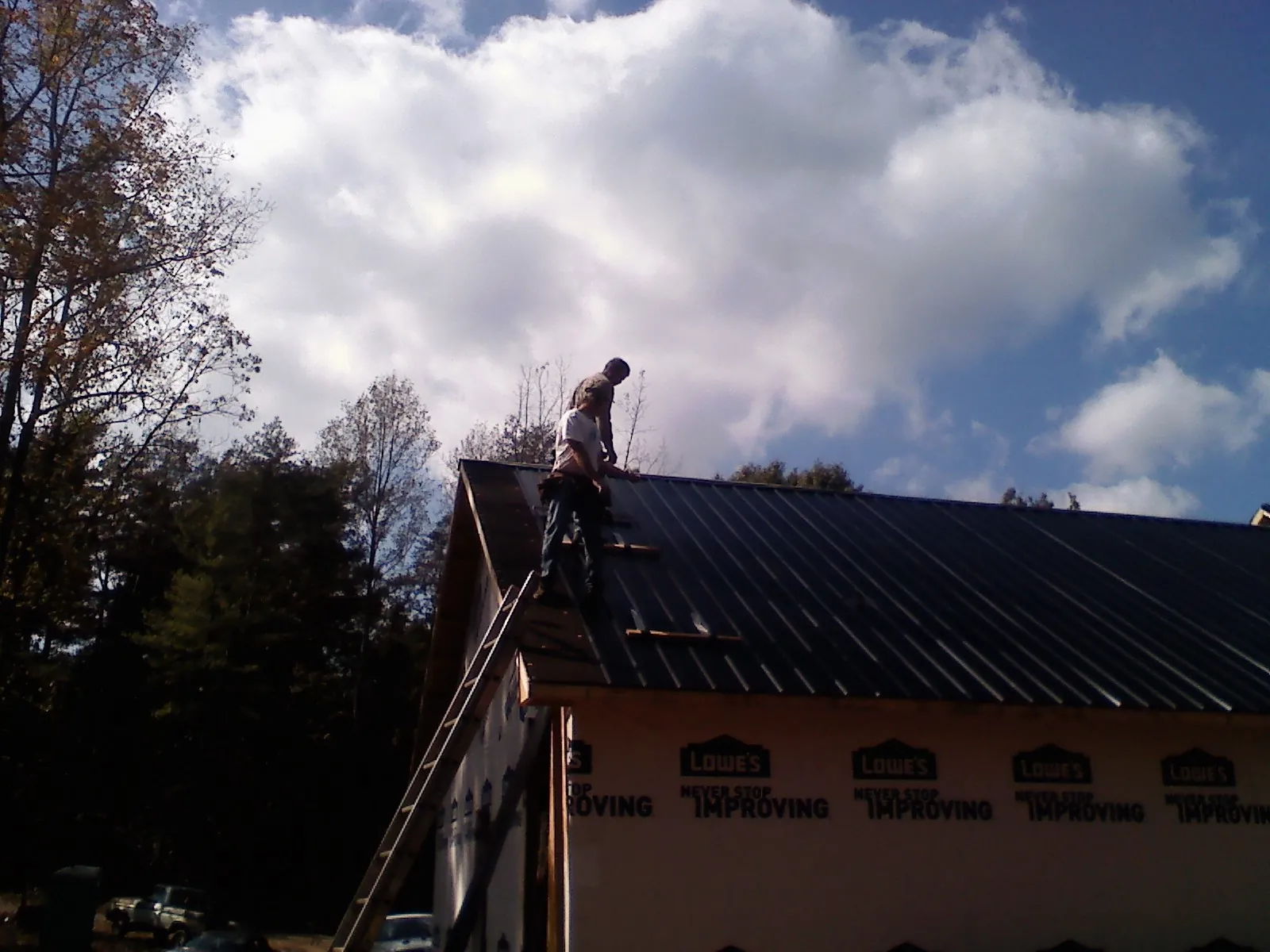 Roofer fastening dark metal panels high against a cloudy sky, from a Roof Inspection job in Oakes