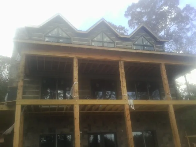 Dormers and porch framing on a large log home under construction — Roof Coating work by our crew in Oakes